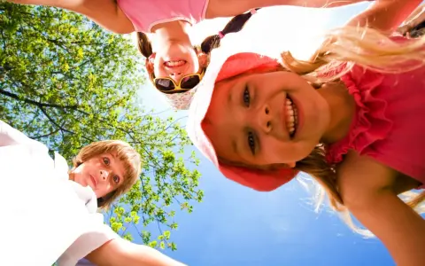 Trois enfants souriants, vus d'en bas, profitent d'une journée ensoleillée lors d'un camp sportif.
