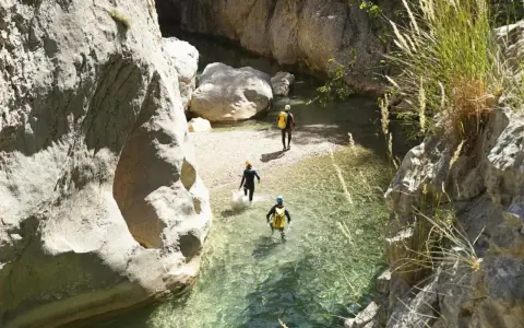 Trois personnes en combinaison font du canyoning dans une rivière aux eaux claires, entourées de falaises rocheuses.