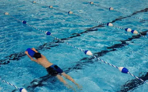 Un nageur utilise une planche bleue dans une piscine avec des lignes de bouées bleues et blanches.