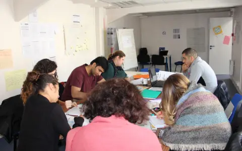 Groupe de personnes assises autour d'une table, travaillant sur des documents et un ordinateur portable.