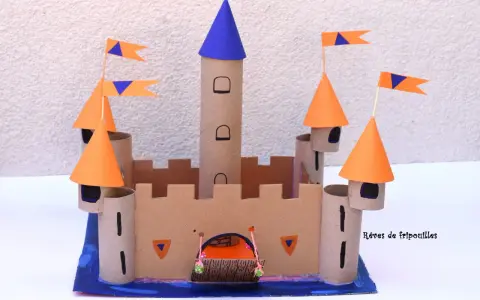 Château fort en carton avec tours, drapeaux orange et bleus, et une herse.