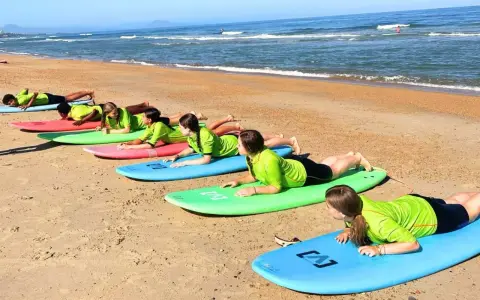 Des adolescents en stage sportif sur la plage, allongés sur des planches de surf, apprenant les bases avant de se jeter à l'eau.