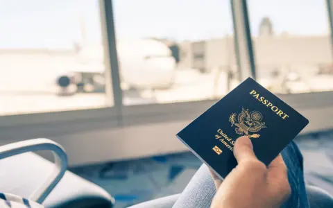 Main tenant une carte d'identité américaine devant une fenêtre d'aéroport avec un avion en arrière-plan.