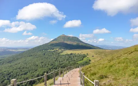 Escalier en bois menant au Puy de Dôme sous un ciel bleu et nuageux.