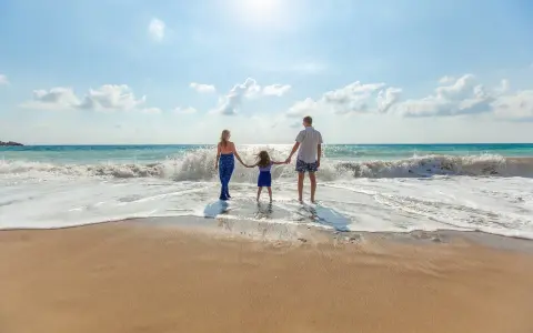Une famille se tient la main sur la plage, profitant des vagues. Ils pensent à devenir famille d'accueil pour les vacances, offrant ces moments de bonheur.