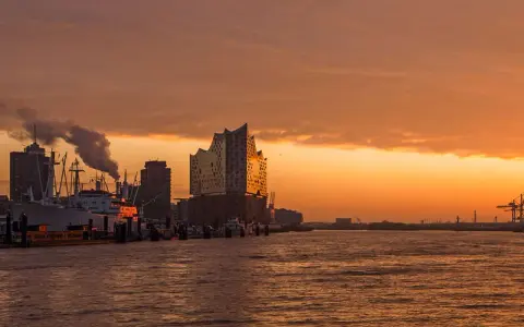 Coucher de soleil sur le port de Hambourg, idéal pour visiter Hambourg en 3 jours. Bateaux, grues et la Philharmonie de l'Elbe se reflètent sur l'eau.