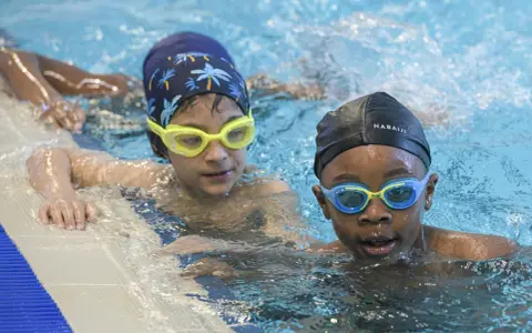 Deux enfants avec des bonnets et lunettes de natation dans une piscine.