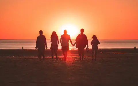 Une famille profite de ses vacances à l'étranger, marchant main dans la main sur une plage au coucher du soleil.