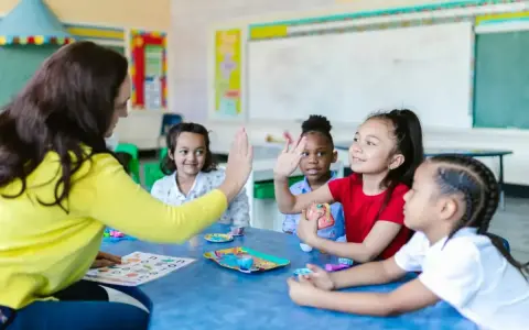 Une enseignante donne une tape dans la main à des enfants autour d'une table dans une salle de classe.