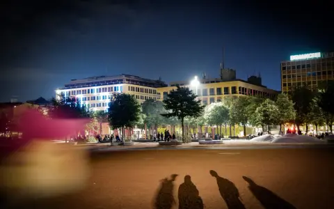 Ombre d'un mineur dehors la nuit, projetées sur une place éclairée par des bâtiments modernes.