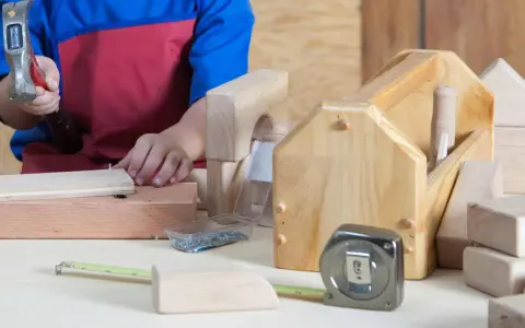 Enfant bricolant avec un marteau, des clous, un mètre ruban et des outils en bois.