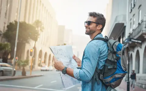 Un homme souriant avec un sac à dos consulte une carte, prêt pour un voyage en immersion dans la ville.