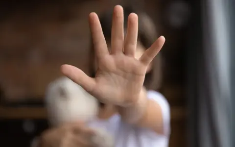 Main d'enfant tendue, stop. Un doudou flou à côté. Une image qui évoque une cellule enfance en danger.