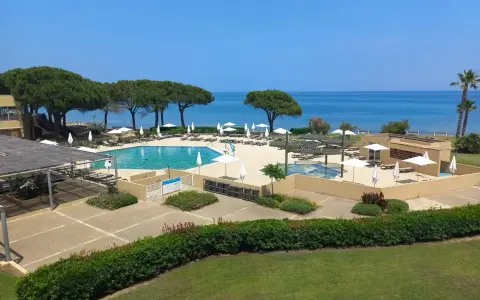 Piscine et transats dans un complexe hôtelier en bord de mer, sous un ciel bleu.