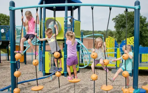 Enfants jouant sur une structure d'escalade avec des cordes et des balles oranges.