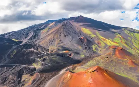 Vue aérienne de l'Etna, avec ses cratères rouges et ses pentes noires et vertes.