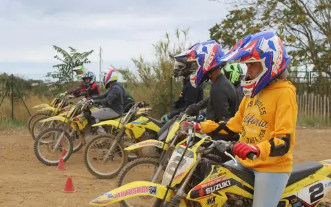 Jeunes pilotes prêts pour une course de moto cross. Casques colorés et motos jaunes alignées.