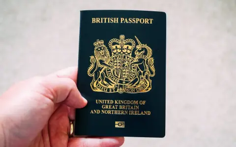 Main d'une personne tenant un passeport britannique bleu foncé avec le blason royal doré.