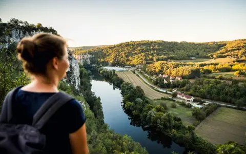 Une femme admire un paysage de carte postale lors de son voyage découverte en France. La rivière serpente à travers des collines verdoyantes et des villages pittoresques.