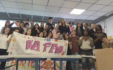 Un groupe d'étudiants pose derrière une banderole "BAFA" décorée de dessins et de fleurs.