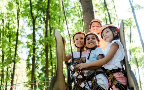 Quatre enfants souriants portant des casques de sécurité dans un parc d'aventure.