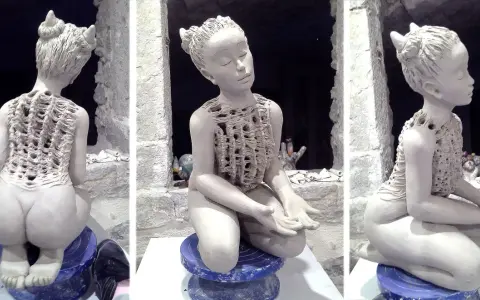 Sculpture en argile d'une jeune fille aux cornes, assise, vêtue d'une tunique ajourée.