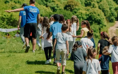 Un groupe d'enfants suit un coach sur une colline verdoyante. Ces actions pour financer un voyage scolaire sont pleines d'énergie et de joie.