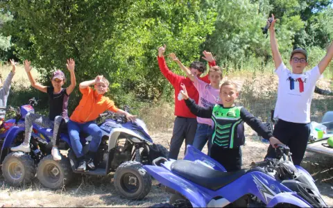Des enfants joyeux sur des quads, bras levés, en extérieur.