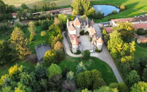 Vue aérienne d'un château entouré d'arbres, avec un étang et un terrain de sport.