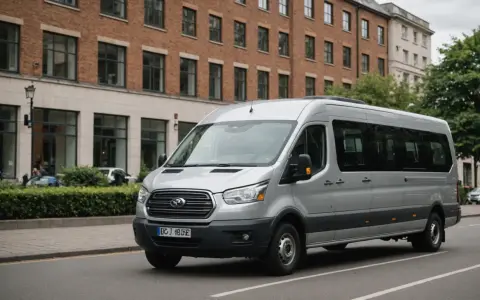 Un homme est au volant, prêt à conduire un minibus argenté dans une rue bordée d'arbres et de bâtiments.