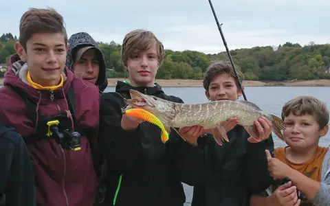 Des jeunes pêcheurs fiers de leur prise lors d'une colonie de vacances pêche. Un beau brochet exhibé devant un lac.