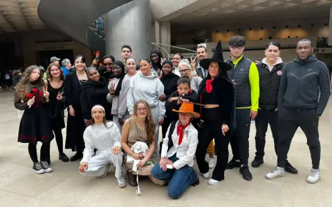 Un groupe de jeunes gens, certains déguisés, pose pour une photo dans un hall moderne.