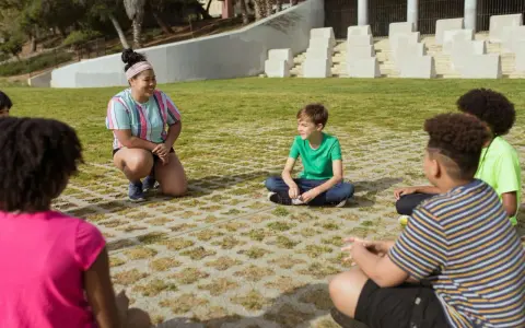 Une animatrice discute avec des enfants assis en cercle dans un parc.