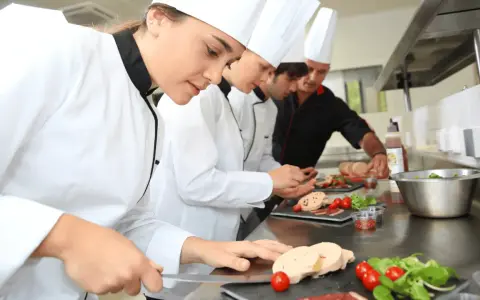 Des chefs apprennent la réglementation atelier cuisine en préparant des mets. Ils coupent du foie gras, des tomates cerises et de la salade.