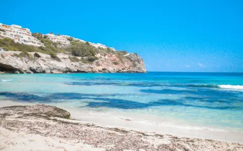 Plage de Majorque avec eaux turquoises, falaises et bâtiments blancs à flanc de colline.