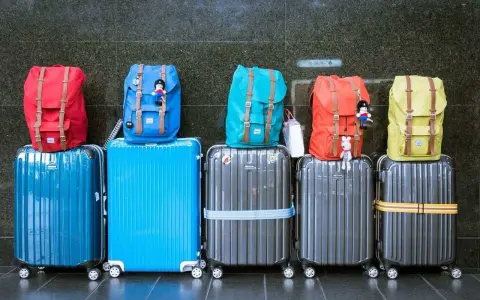 Six valises de différentes couleurs empilées, avec des sacs à dos colorés sur le dessus.
