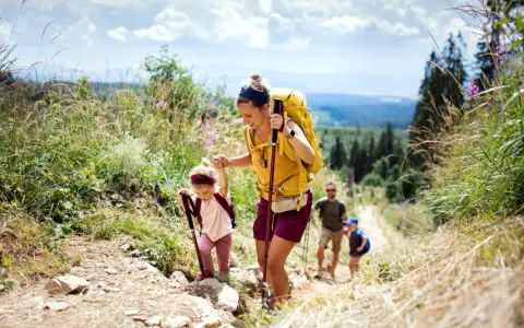 Famille faisant de la randonnée en montagne, une mère aide sa fille à monter un sentier.
