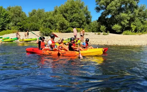 Des personnes profitent d'une activité canoe kayak sur une rivière ensoleillée, entourées de verdure et d'une plage de galets.