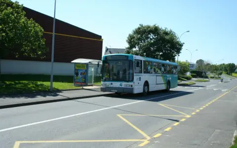 Un bus scolaire s'arrête à un arrêt de bus, respectant le code de la route. Le soleil brille sur la route.
