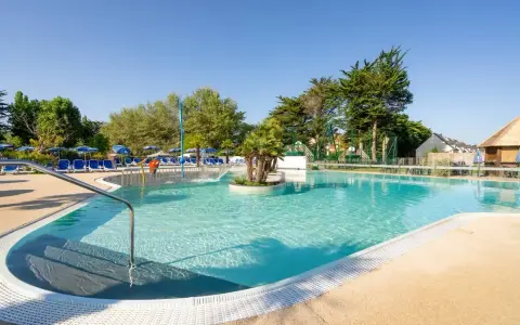 Piscine extérieure avec chaises longues bleues, parasols et végétation luxuriante sous un ciel bleu clair.