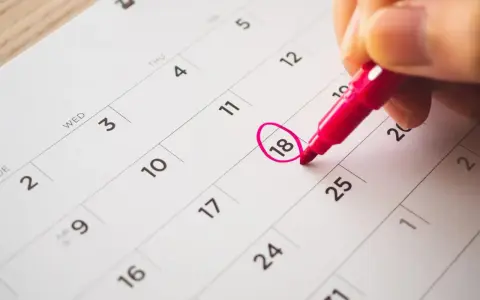 Une main entoure le 18 sur un calendrier, marquant le début des vacances scolaires à Fribourg.