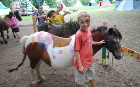 Enfants avec des poneys décorés de peinture, dans un campement avec des tentes.