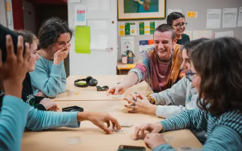 Des jeunes rient en jouant à un jeu de cartes autour d'une table.