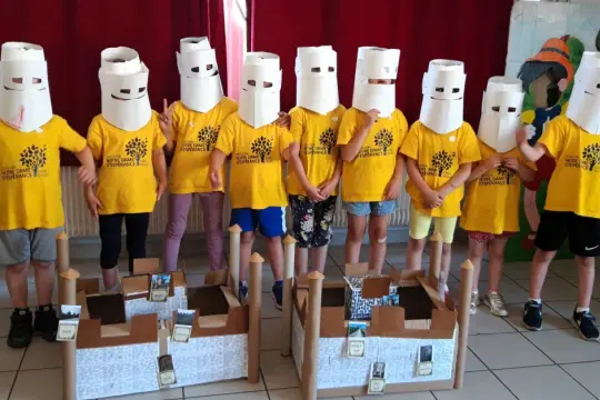 Des enfants costumés en chevaliers, prêts pour un séjour immersion médiéval, posent devant des maquettes de châteaux.