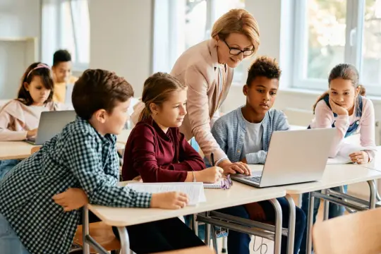 Enseignante aidant des élèves sur un projet d'accueil individualisé avec des ordinateurs en classe.