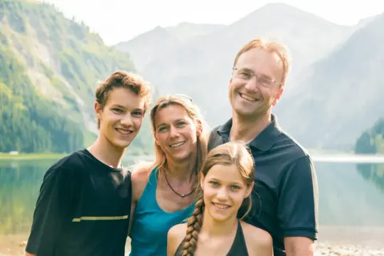 Famille souriante au bord d'un lac, paysage montagneux. Une belle idée pour savoir comment partir en famille d'accueil.