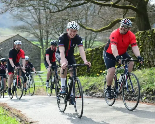 Un groupe de cyclistes souriants roule sur une route de campagne, respectant le code de la route pour cycliste en groupe.
