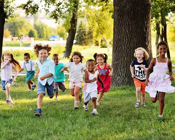 Des enfants joyeux courent dans l'herbe, profitant d'une journée ensoleillée dans une colonie de vacances 3-6 ans.
