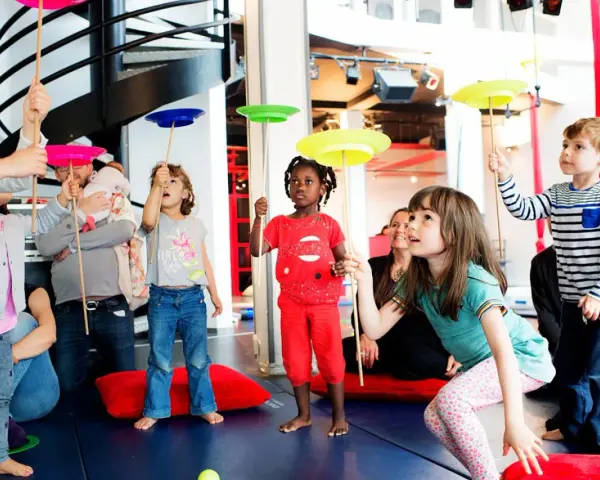 Des enfants apprennent à faire tourner des assiettes sur des bâtons lors d'un atelier cirque.