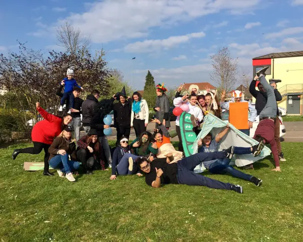 Groupe de jeunes en costumes et déguisements, certains sur une tente, sur l'herbe par beau temps.